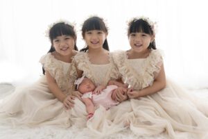 Three Asian girls in white dresses posing for a photo captured by a Miami newborn photographer.