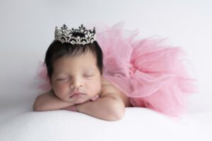 Newborn baby wearing a sparkling tiara and a pink tulle skirt, lying on a soft white surface with eyes closed, captured beautifully by a Miami newborn photographer.