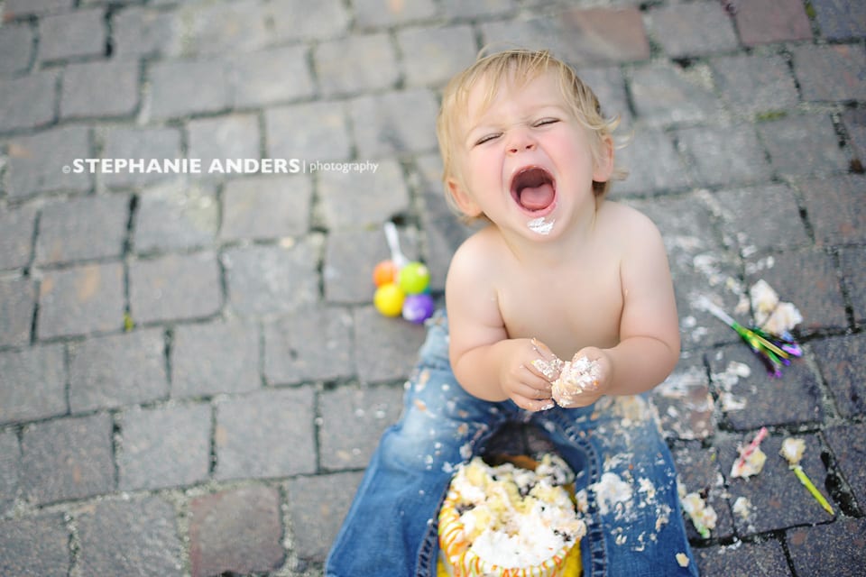 happy baby boy eating messy cake on stone driveway