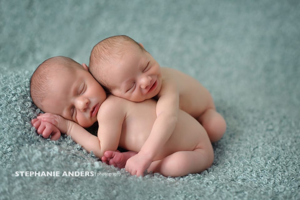 newborn twins hugging each other with smiles