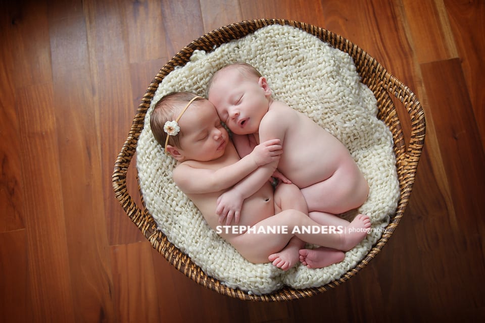 newborn twins cuddling in basket on wood floor