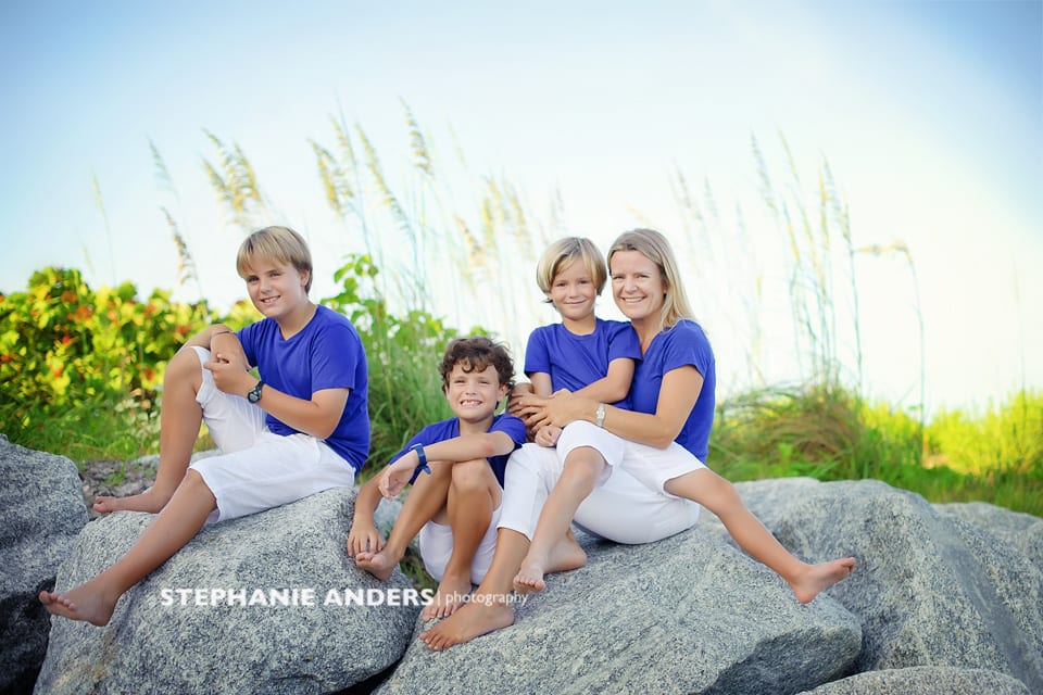mom and three kids sitting on rocks at beach
