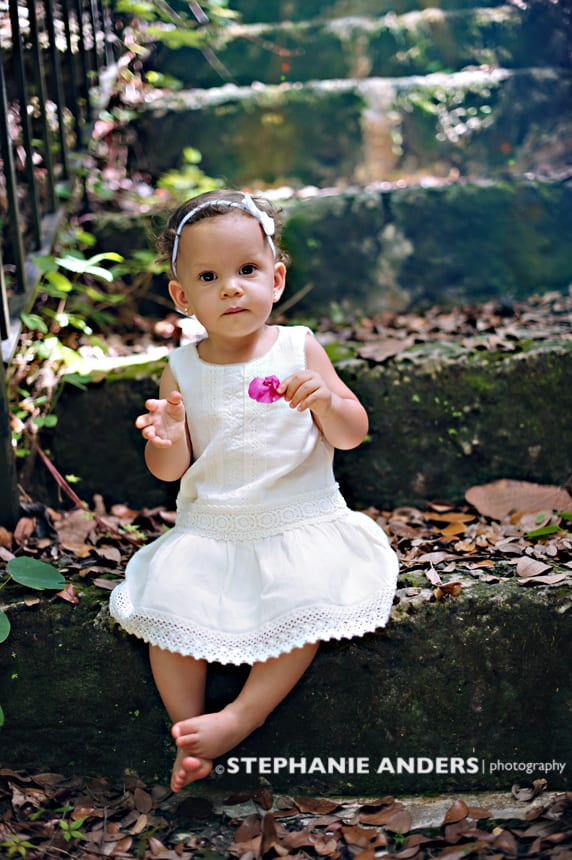 small girl holding pink flower wearing white dress