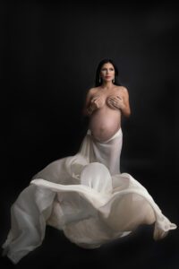A pregnant woman in a white dress posing on a black background.