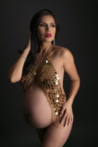 A pregnant woman in a gold sequined outfit posing for a photo.