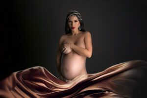 A creatively accessorized pregnant woman posing on a dark background.