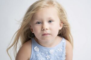 A little girl in a blue dress is posing for childhood portraits.