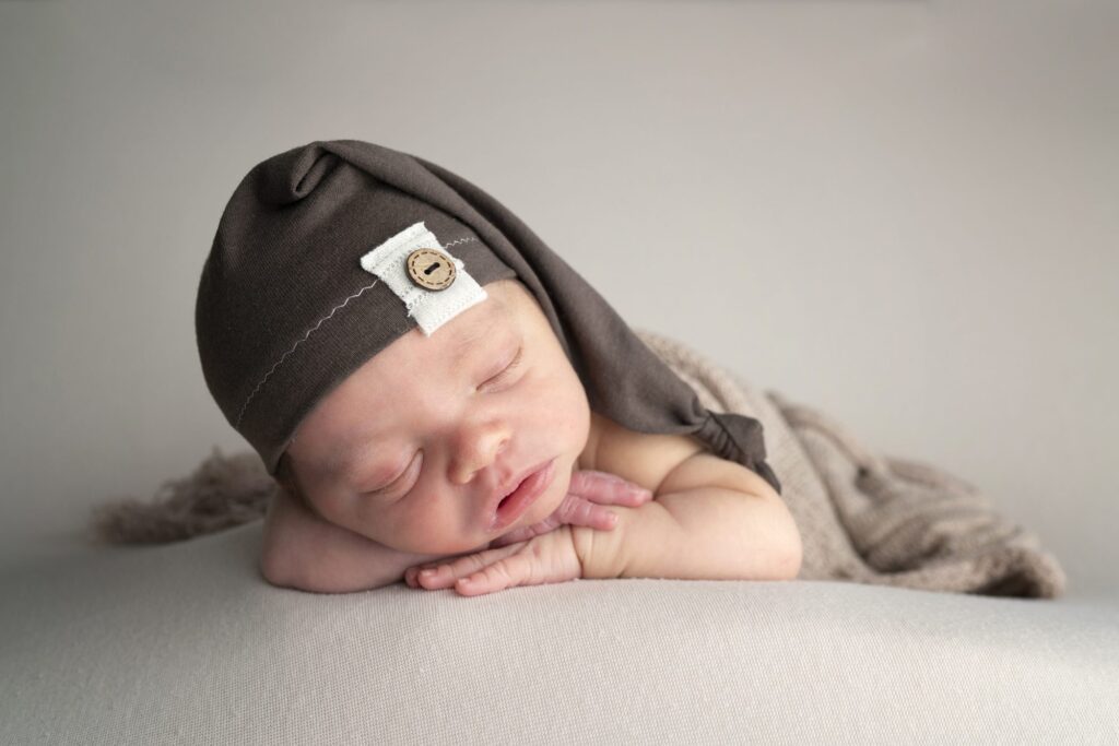 A newborn wearing a hat sleeps on a blanket.