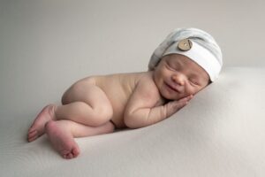 A newborn baby boy wearing a white hat is comfortably lying on a white background.