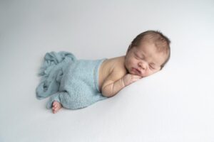 A smiling newborn wrapped in a blue blanket.
