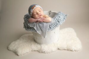 A smiling newborn baby sleeping in a bucket.