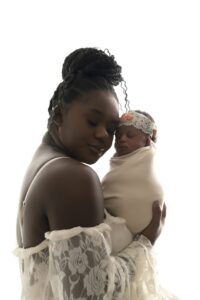A woman in a white lace top holds a swaddled newborn baby wearing a headband, both against a white background.