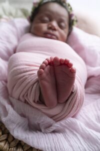 A newborn baby wrapped in a pink blanket sleeps on their back, with the focus on their feet in the foreground.