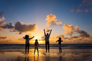 Four people jumping on a beach at sunset with clouds in the sky and the sun low above the horizon, capturing the joyful spirit of fall family photos in Miami.