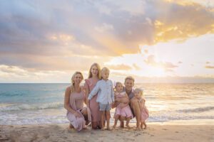 A family of six poses on a sandy beach at sunset with the ocean and a cloudy sky in the background, capturing memories during the best time for family photos in Miami.